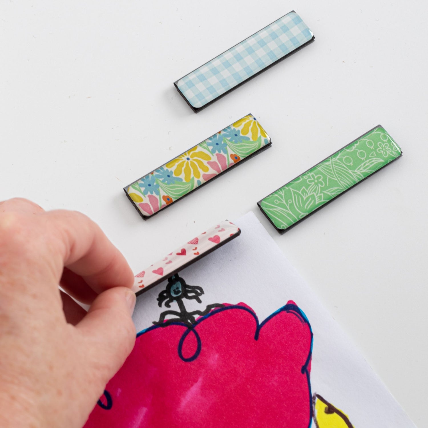 Colorful rectangular art clips on a white background with a hand holding one of them.